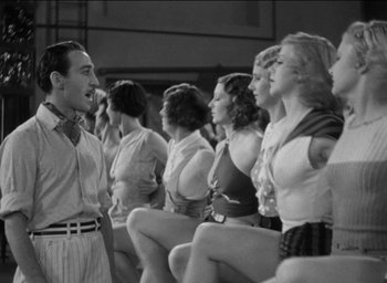Movie still from “42nd Street” (1933), directed by Lloyd Bacon – A man talking to a group of women in front of a wall; Medium shot, Low angle