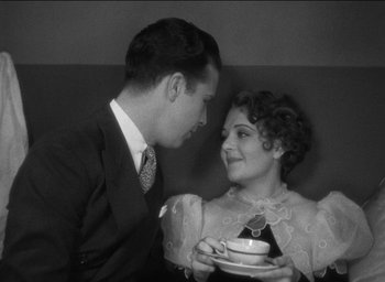 Movie still from “42nd Street” (1933), directed by Lloyd Bacon – A man and a woman are holding a cup of tea; Medium shot, High angle