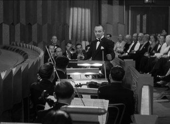 Movie still from “42nd Street” (1933), directed by Lloyd Bacon – An orchestra conductor leading a performance in front of an audience; Wide shot, High angle