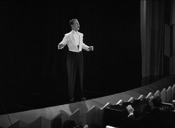 Movie still from “42nd Street” (1933), directed by Lloyd Bacon – A person on a stage singing into a microphone; Wide shot, High angle