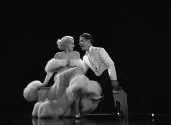 Movie still from “42nd Street” (1933), directed by Lloyd Bacon – A man and a woman are sitting on a bench in front of each other on a stage; Wide shot, High angle
