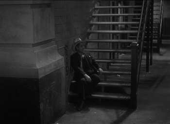 Movie still from “42nd Street” (1933), directed by Lloyd Bacon – A black and white photo of a man sitting on some steps; Wide shot, High angle