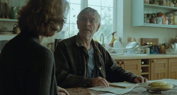 Movie still from “45 Years” (2015), directed by Andrew Haigh – An older man sitting at a table with a woman looking at papers; Medium shot, Over the shoulder angle