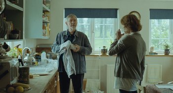 Movie still from “45 Years” (2015), directed by Andrew Haigh – An older man holding a towel in front of a woman in a kitchen; Medium shot, Over the shoulder angle