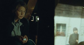 Movie still from “45 Years” (2015), directed by Andrew Haigh – A person sitting in a chair holding a remote control; Medium shot, Low angle