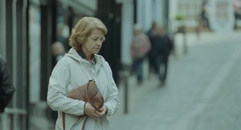 Movie still from “45 Years” (2015), directed by Andrew Haigh – An older woman holding a purse while standing on the sidewalk; Medium shot, Over the shoulder angle