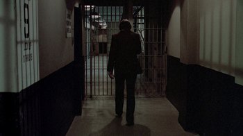 Movie still from “48 Hrs.” (1982), directed by Walter Hill – A man in a suit walking through a jail cell; Wide shot, High angle