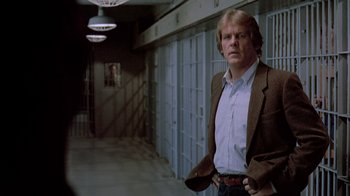 Movie still from “48 Hrs.” (1982), directed by Walter Hill – A man standing in a hallway with his hands in his pockets; Medium shot, Over the shoulder angle