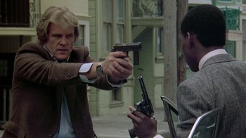 Movie still from “48 Hrs.” (1982), directed by Walter Hill – Two men are holding guns and one is pointing a gun at the other; Medium shot, Over the shoulder angle