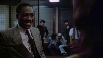 Movie still from “48 Hrs.” (1982), directed by Walter Hill – A man in a suit and tie on a train; Medium shot, Over the shoulder angle
