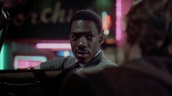 Movie still from “48 Hrs.” (1982), directed by Walter Hill – A man in a suit and tie sitting in front of a neon sign; Close Up shot, Over the shoulder angle