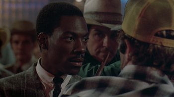 Movie still from “48 Hrs.” (1982), directed by Walter Hill – A group of men standing next to each other in a room; Close Up shot, Over the shoulder angle