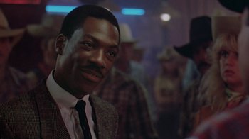 Movie still from “48 Hrs.” (1982), directed by Walter Hill – A man wearing a suit and tie in front of a group of people; Close Up shot, Over the shoulder angle