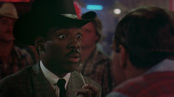 Movie still from “48 Hrs.” (1982), directed by Walter Hill – A man wearing a top hat talking to another man in a suit; Close Up shot, Over the shoulder angle