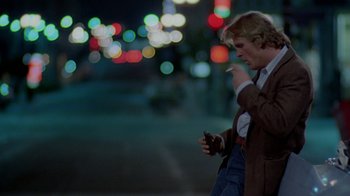 Movie still from “48 Hrs.” (1982), directed by Walter Hill – A man standing on the side of the road while looking at his cell phone; Wide shot, Low angle