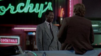 Movie still from “48 Hrs.” (1982), directed by Walter Hill – A man in a suit and tie standing next to another man in a suit and tie; Medium shot, Over the shoulder angle