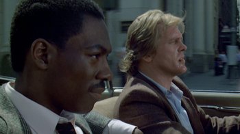 Movie still from “48 Hrs.” (1982), directed by Walter Hill – Two men sitting next to each other on a couch; Close Up shot, Low angle