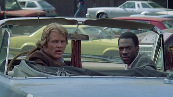 Movie still from “48 Hrs.” (1982), directed by Walter Hill – Two people in a car with a helicopter on the windshield; Medium shot, Over the shoulder angle