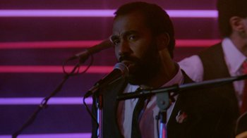 Movie still from “48 Hrs.” (1982), directed by Walter Hill – A man in a suit and tie is speaking into a microphone; Close Up shot, Low angle