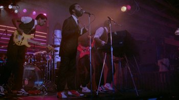 Movie still from “48 Hrs.” (1982), directed by Walter Hill – A group of people on a stage with a microphone; Wide shot, Low angle