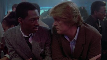 Movie still from “48 Hrs.” (1982), directed by Walter Hill – Two men in suits talking to each other in a room; Close Up shot, Over the shoulder angle