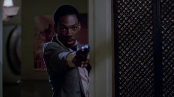 Movie still from “48 Hrs.” (1982), directed by Walter Hill – A man in a suit and tie points a gun at the camera; Close Up shot, Over the shoulder angle