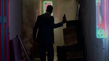Movie still from “48 Hrs.” (1982), directed by Walter Hill – A man in a suit holding a gun in a dark room; Wide shot, Low angle