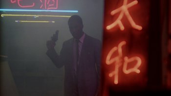Movie still from “48 Hrs.” (1982), directed by Walter Hill – A man in a suit and tie holding a cell phone in front of a neon sign; Wide shot, Low angle