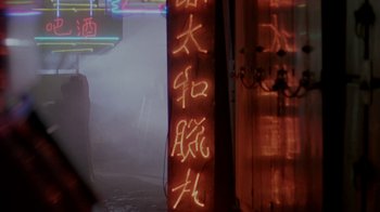Movie still from “48 Hrs.” (1982), directed by Walter Hill – A person walking in the rain next to a building with neon signs; Wide shot, Over the shoulder angle