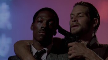 Movie still from “48 Hrs.” (1982), directed by Walter Hill – A man with a gun in front of a man with a tie; Close Up shot, Low angle