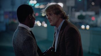 Movie still from “48 Hrs.” (1982), directed by Walter Hill – Two men in business suits talking to each other; Medium shot, Over the shoulder angle