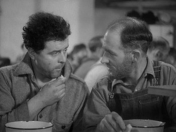 Movie still from “49th Parallel” (1941), directed by Michael Powell – A couple of men sitting next to each other at a table; Medium shot, Over the shoulder angle