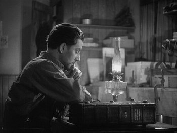 Movie still from “49th Parallel” (1941), directed by Michael Powell – A black and white photo of a man sitting in front of an oil lamp; Medium shot, High angle