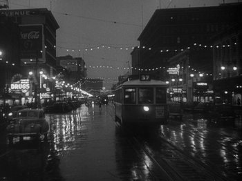 Movie still from “49th Parallel” (1941), directed by Michael Powell – A black - and - white photo of a city street at night; Extreme Wide shot, High angle