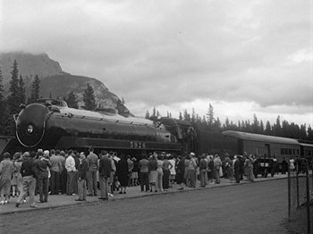 Movie still from “49th Parallel” (1941), directed by Michael Powell – A crowd of people standing next to a train on the side of the road; Extreme Wide shot, High angle