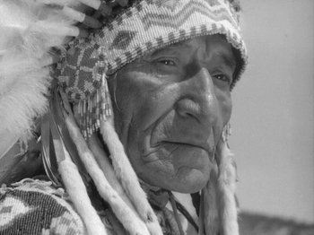 Movie still from “49th Parallel” (1941), directed by Michael Powell – An old man wearing a headdress with feathers on his head; Close Up shot, Low angle