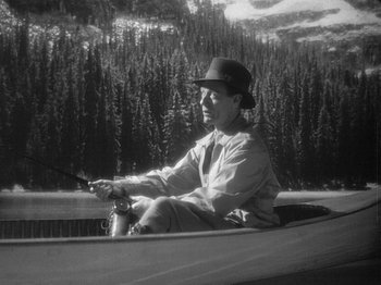 Movie still from “49th Parallel” (1941), directed by Michael Powell – A man in a hat is sitting in a boat holding a fishing rod; Medium shot, High angle