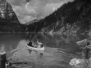 Movie still from “49th Parallel” (1941), directed by Michael Powell – Two people are in a canoe on a lake near mountains; Extreme Wide shot, High angle