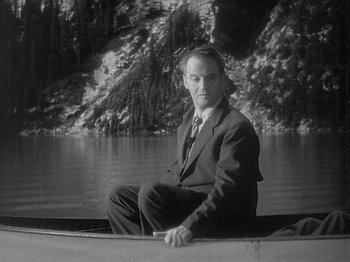 Movie still from “49th Parallel” (1941), directed by Michael Powell – A black and white photo of a man sitting on a boat in the water; Medium shot, High angle