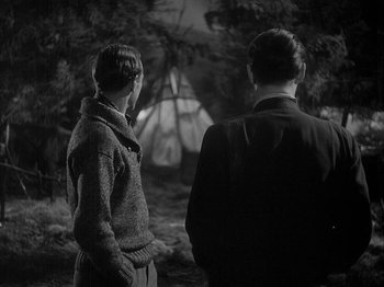 Movie still from “49th Parallel” (1941), directed by Michael Powell – Two people standing in front of a forest at night; Medium shot, Over the shoulder angle