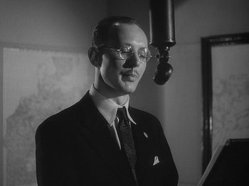 Movie still from “49th Parallel” (1941), directed by Michael Powell – A man in a suit and tie standing in front of a microphone; Close Up shot, Low angle
