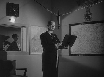 Movie still from “49th Parallel” (1941), directed by Michael Powell – A black and white photo of a man standing at a podium with a lap top computer; Medium shot, Low angle
