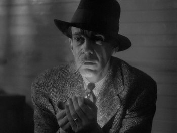Movie still from “49th Parallel” (1941), directed by Michael Powell – An older man wearing a suit and a hat smoking a cigarette; Close Up shot, Low angle