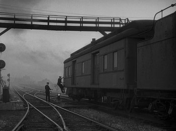 Movie still from “49th Parallel” (1941), directed by Michael Powell – Two people standing on a train track next to train cars; Extreme Wide shot, Low angle