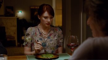 Movie still from “50/50” (2011), directed by Jonathan Levine – A woman sitting at a table with a plate of food in front of her; Medium shot, Over the shoulder angle