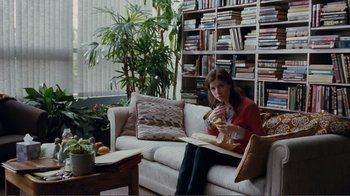 Movie still from “50/50” (2011), directed by Jonathan Levine – A woman sitting on top of a white couch eating a sandwich; Wide shot, Over the shoulder angle