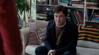 Movie still from “50/50” (2011), directed by Jonathan Levine – A man sitting on top of a couch in a living room; Medium shot, Over the shoulder angle