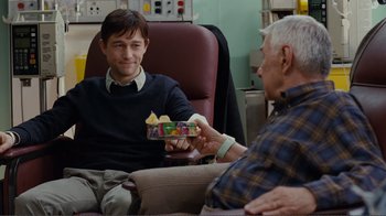 Movie still from “50/50” (2011), directed by Jonathan Levine – A man sitting in front of another man holding a box of cookies; Medium shot, Over the shoulder angle