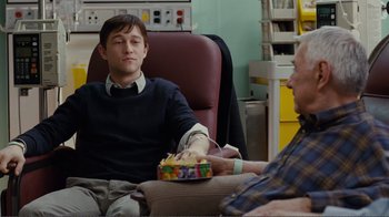 Movie still from “50/50” (2011), directed by Jonathan Levine – A man sitting in a chair holding a box of candy; Medium shot, Over the shoulder angle