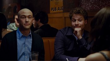 Movie still from “50/50” (2011), directed by Jonathan Levine – Two men sitting at a table in front of a sign; Medium shot, Over the shoulder angle